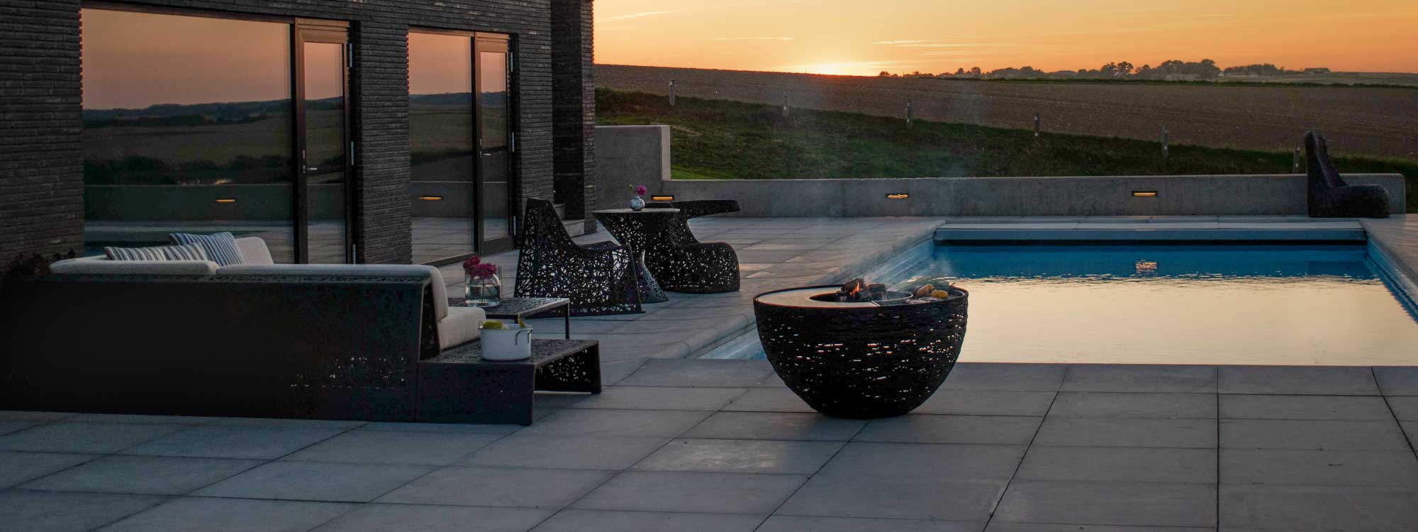 Image of wafts of smoke & smells rising from food cooking on Lava Nest BBQ and fire pit by Unknown Nordic, shown on poolside at dusk