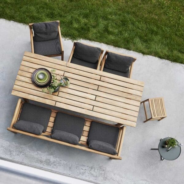 Image of birds eye view of Grace teak dining table, chairs and bench by Cane-line, on poured concrete terrace next to lawn,