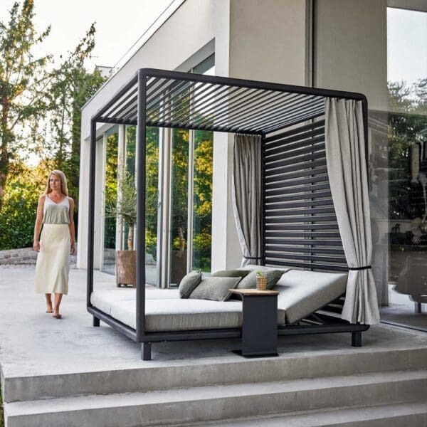 Image of woman on terrace next to Laze garden daybed with roof and curtains by Cane-line