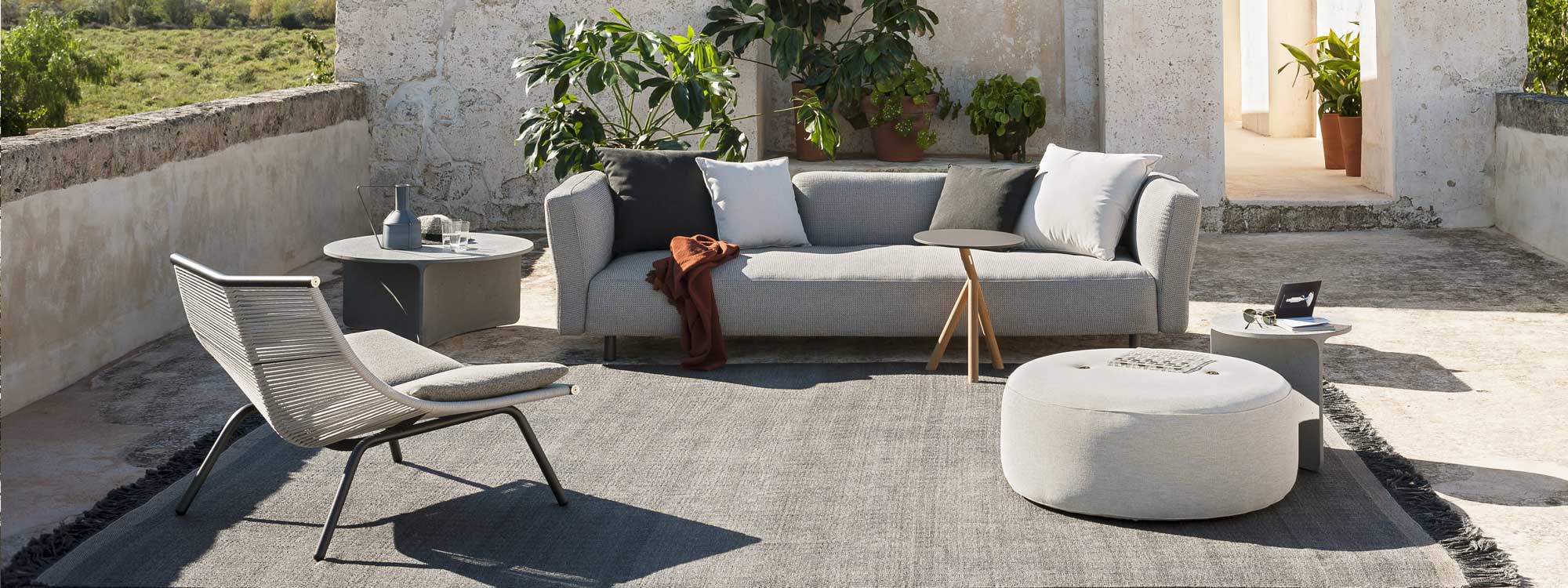 Image of RODA Mamba luxury garden sofa, Laze modern lounge chair and Aspic concrete garden table, shown on rustic Italian courtyard