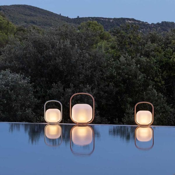 Image at dusk of lit Todus Otus modern outdoor lanterns on poolside, with their reflection in water below