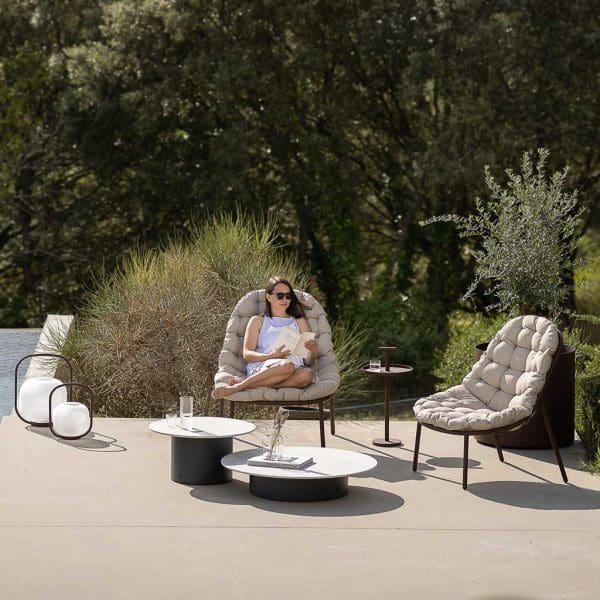 Image of woman sat reading on Alba modern outdoor lounge chair on terrace, with Otus lamps and Baza low tables
