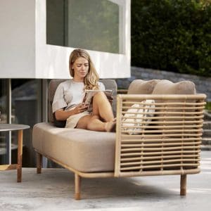 Image of a woman lying down, reading on Sense cane garden sofa by Cane-line