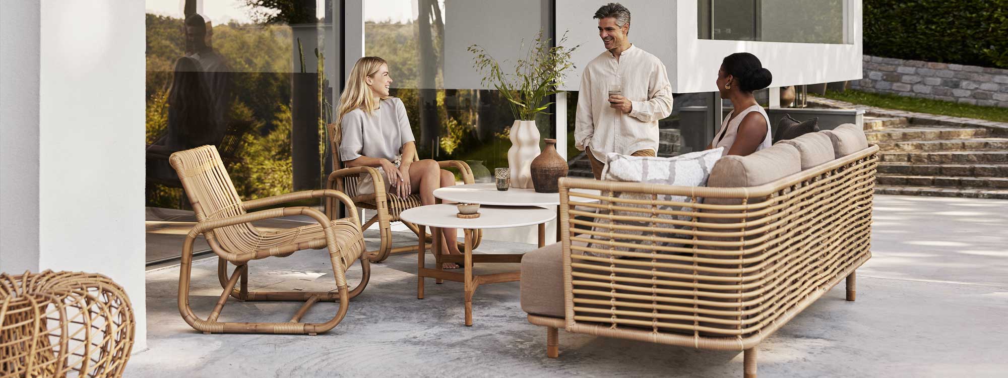 Image of 3 people enjoying Sense outdoor cane sofa and Twist teak low table by Cane-line garden furniture