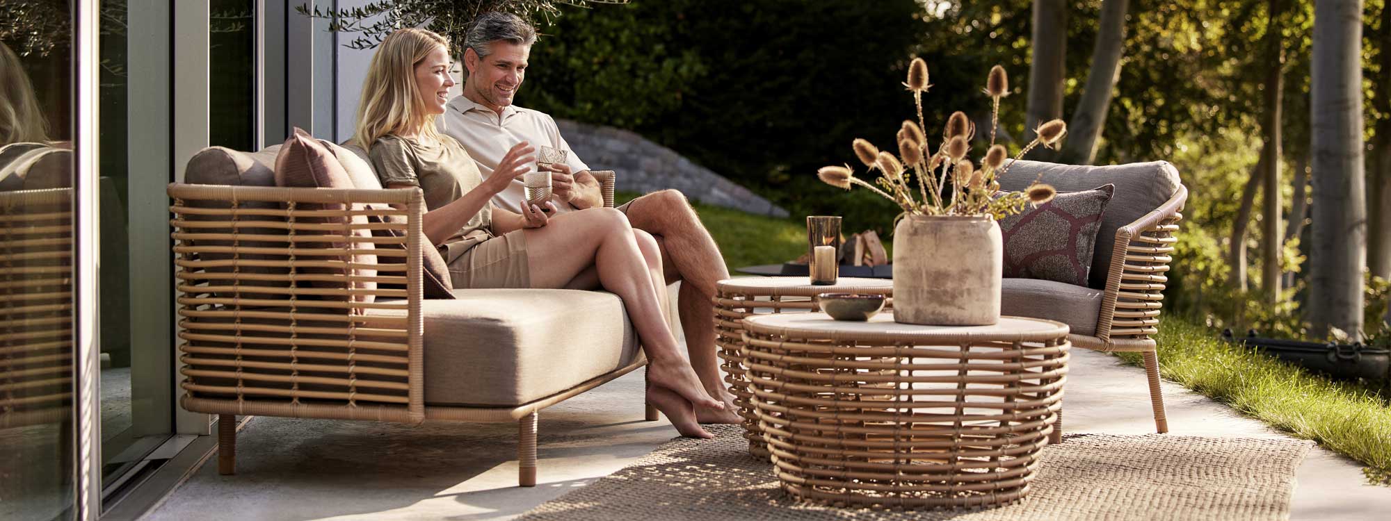 Image of couple sat on Sense synthetic cane sofa next to Basket low table by Cane-line outdoor furniture