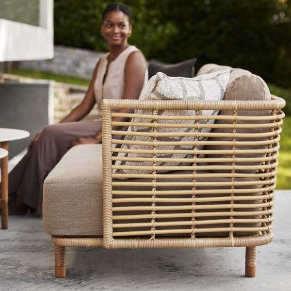 Image of woman sat on Sense cane garden sofa with taupe cushions by Cane-line