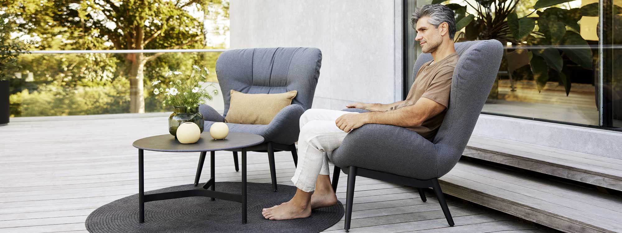 Image of man enjoying the comfort of Serene grey upholstered garden lounge chair by Cane-line