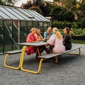 Image of 5 women sat socialising on The Table contemporary picnic set with yellow tubular steel frame and afzelia hardwood surfaces by Wunder, Belgium