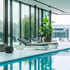 Image of pair of Bari modern sun loungers on interior poolside, with Bari garden sofa outside