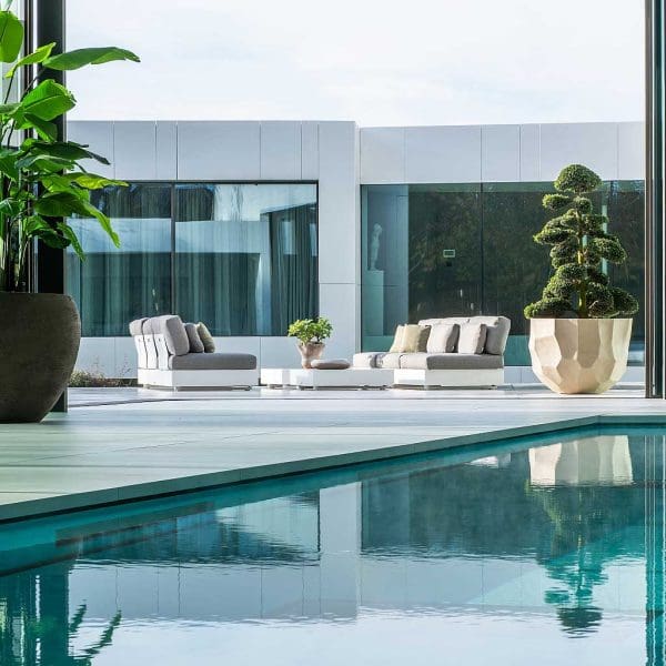 Image of pair of white Bari minimalist exterior sofas on indoor poolside in between 2 large planters with exotic plants