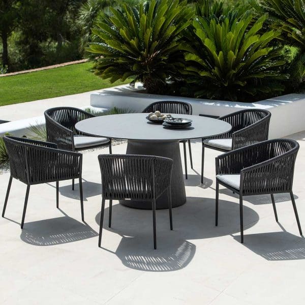 Image of Fortuna Rope black tub dining chairs around a Jati & Kebon circular garden table on sunny terrace, with lawns and exotic plants in the background