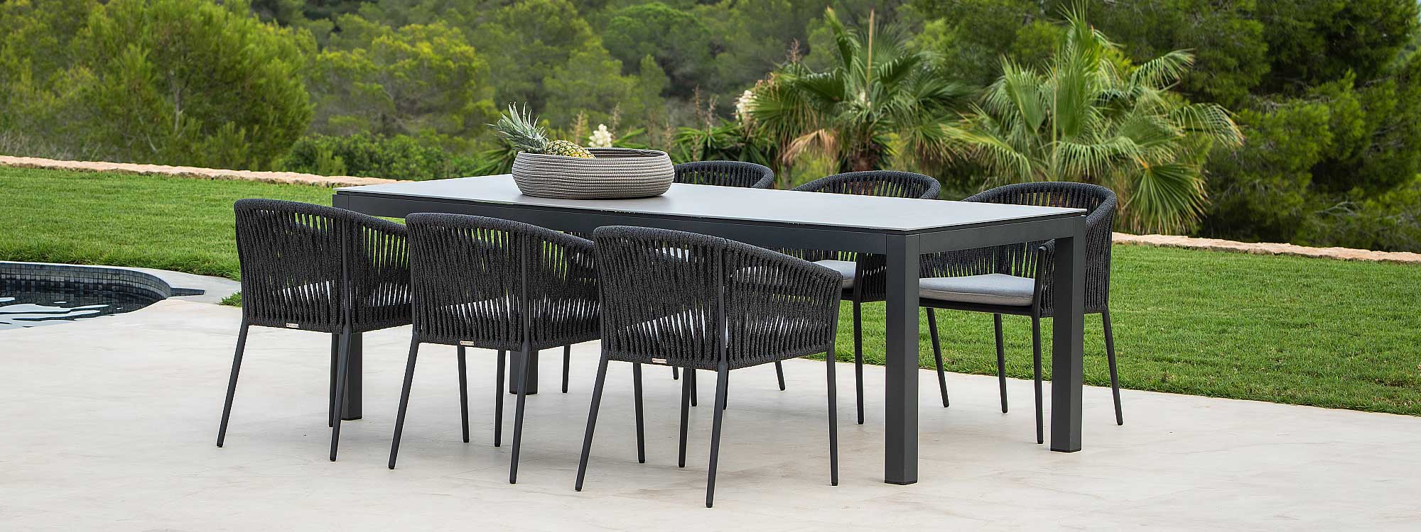 Image of Fortuna Rope black tub garden chairs around Jati & Kebon chunky rectangular garden table, shown on terrace with woodland in the background