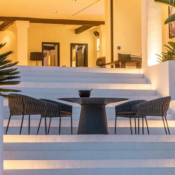 Nighttime image of Fortuna Socks black tub chairs around a circular Jati & Kebon garden table on illuminated white-washed terrace