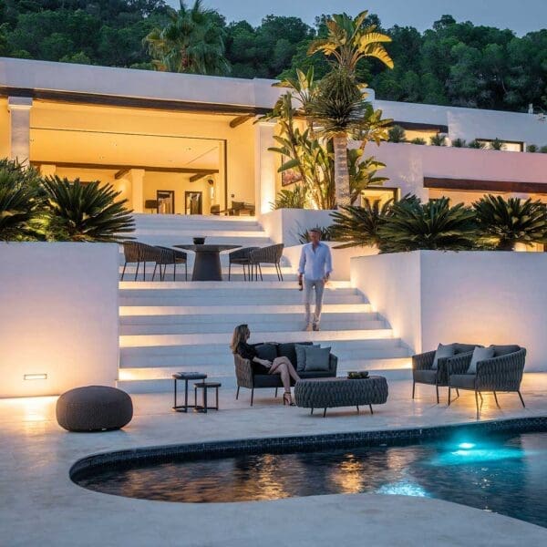 Image of large whitewashed poolside at dusk with Jati & Kebon Fortuna Socks exterior lounge set next to the pool, with Fortuna Socks garden chairs at the top of large flight of stairs in the background