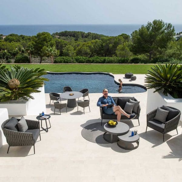 Image of man relaxing in Fortuna Socks garden furniture on sunny poolside, whilst woman lowers herself into the water in the background