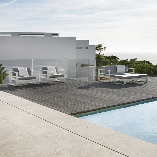 Image of RENO contemporary garden sofa and lounge chairs with white frames and light grey cushions, shown on wooden decked poolside