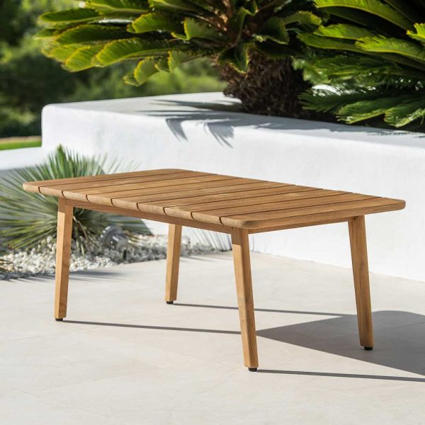 Image of Ritz teak garden table on sunny terrace with whitewashed raise flower bed with palms in background