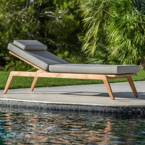 Image of Jati & Kebon Ritz teak sunbed with cushion, shown on sunny poolside with lawn, palm tree and shrubs in background