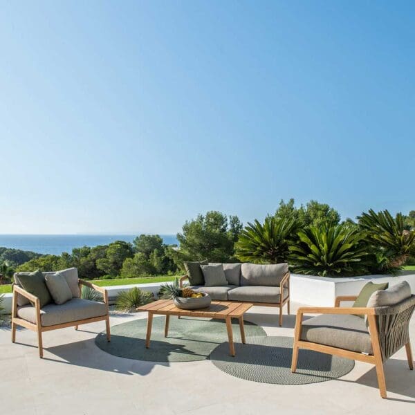 Image of Ritz teak outdoor lounge set on sunny terrace, with palms, lawn, trees and sea in background beneath clear blue sky
