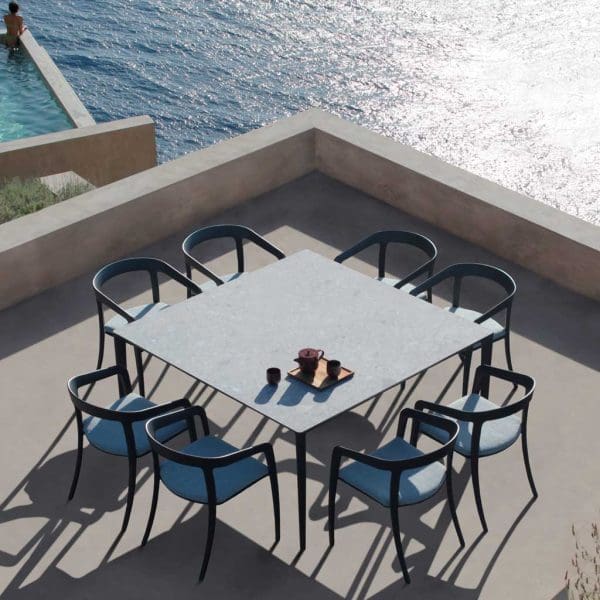 Image of aerial shot of U-nite square garden table with 8 Jive chairs around it, shown on terrace with sea in the background