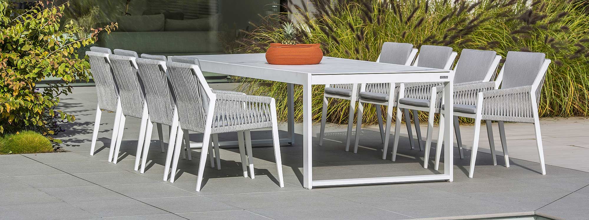 Image of closed Vigo XL white extending garden table with 8 white Ritz contemporary outdoor chairs by Jati & Kebon