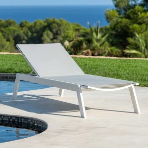 Image of Vigo XL minimalist sunbed on sunny poolside, with lawn, woodland and blue sea and sky in the background