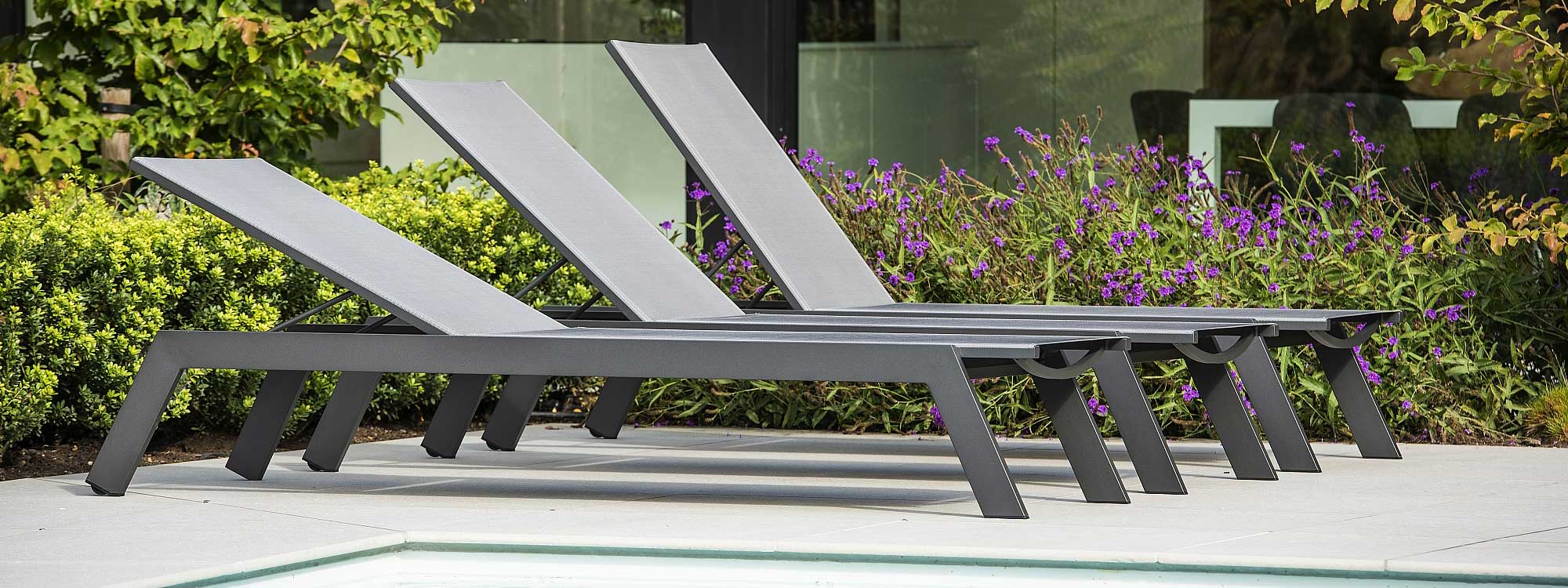 Image of row of 3 Vigo XL adjustable sun loungers with charcoal coloured frames and silver-grey Texteline seat and back rest by Jati & Kebon