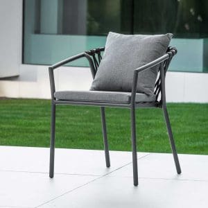 Image of Jati & Kebon's Kapra black garden chair with grey back and seat cushions, shown in terrace with grass and floor to ceiling glass in the background
