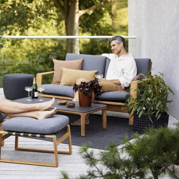 Image of man enjoying glass of wine whilst sat on Endless Soft upholstered teak sofa by Cane-line