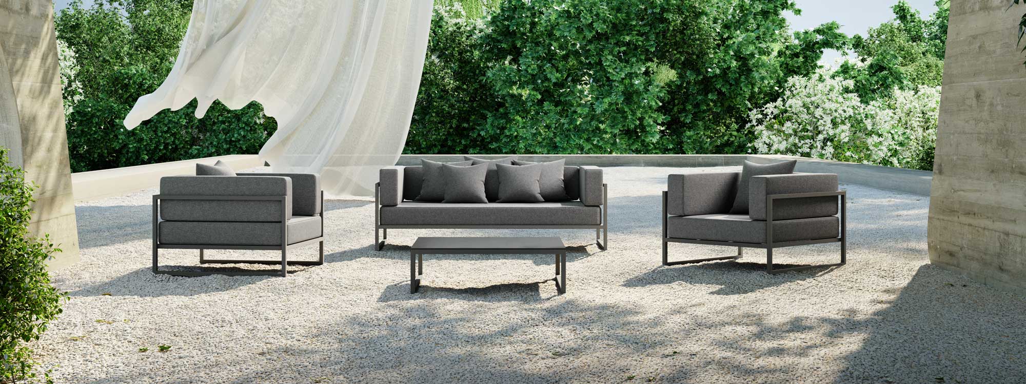 Image of Oiside Línea 2 seat garden sofa and and lounge chairs on large gravel terrace with trees in the background and a white drape being blow in the foreground