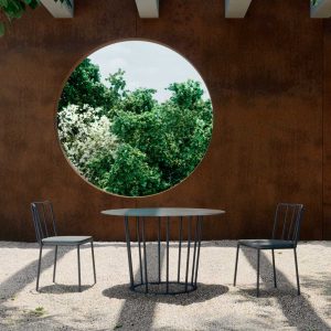 Image of Oiside Panama round garden table and modern outdoor chairs on gravel floor, with large oxidised corten steel wall in the background
