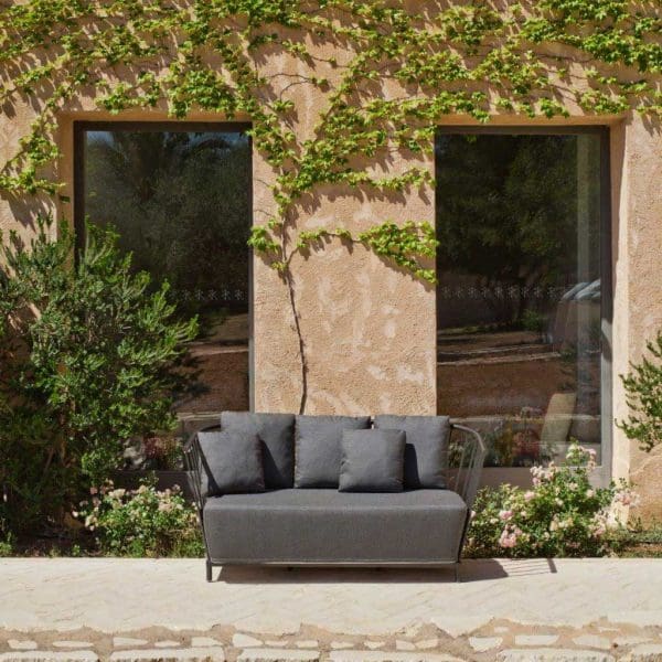 Image of Oiside Panama small garden sofa on sunny terrace, with rustic wall in the background