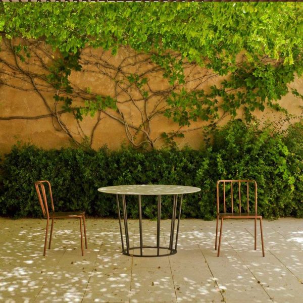 Image of Oiside Panama garden table and chairs in dappled light and shade beneath pergola, with climbing plant growing up the wall in the background