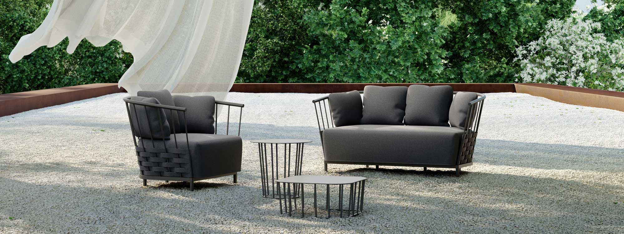 Image of Oiside Panama contemporary 2 seater garden sofa and lounge chair on gravel terrace, with shrubs and trees in the background