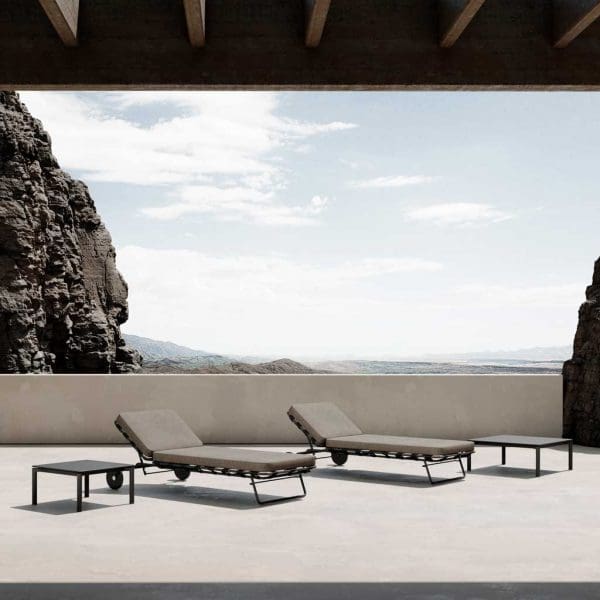Image of pair of Twist modern sun beds and low tables in sleek terrace, with rockface and arid countryside in the background