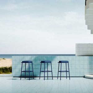 Image of row of 3 Violet upholstered outdoor bar stools by Oiside, shown next to exterior tiled bar counter with sand dunes and blue sky in the background