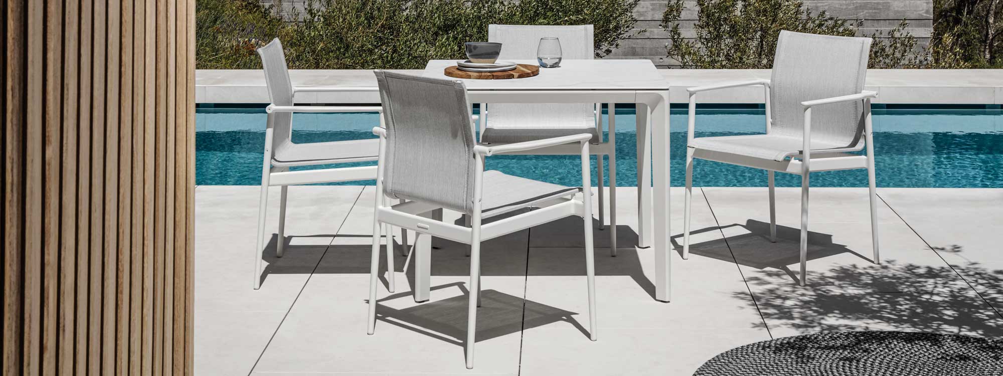 Image of Gloster 180 garden chairs and Carver square garden table with ceramic top, shown on sunny poolside