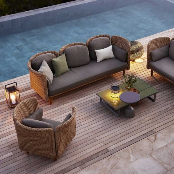 Image at dusk of Arch 3 seat rattan garden sofa and lounge chair by Cane-line on poolside