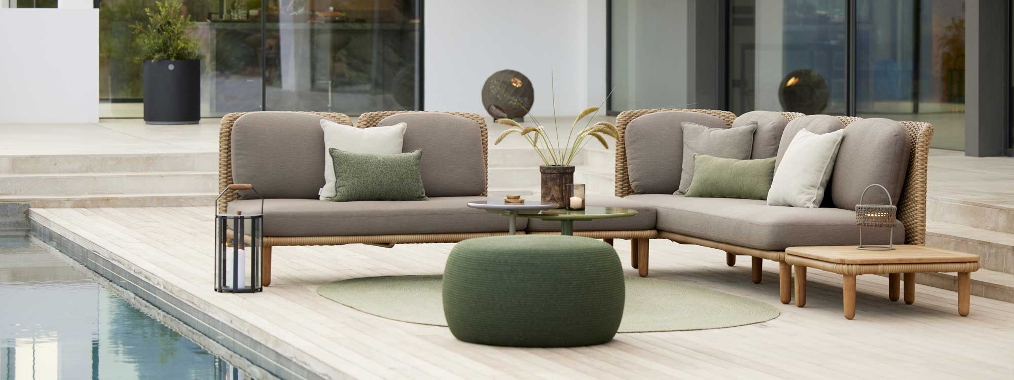 Image of Arch contemporary cane garden corner sofa, together with circle pouf and Glaze low tables by Cane-line, on wooden decked poolside