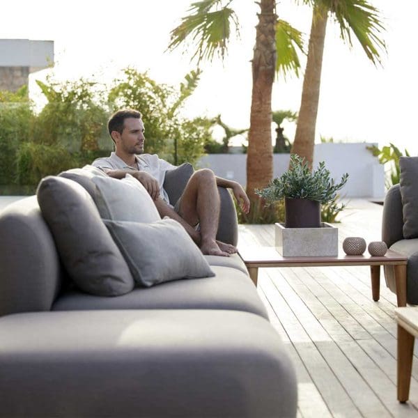 Image of man sat on Cane-line minimalist garden sofa with palm trees in the background