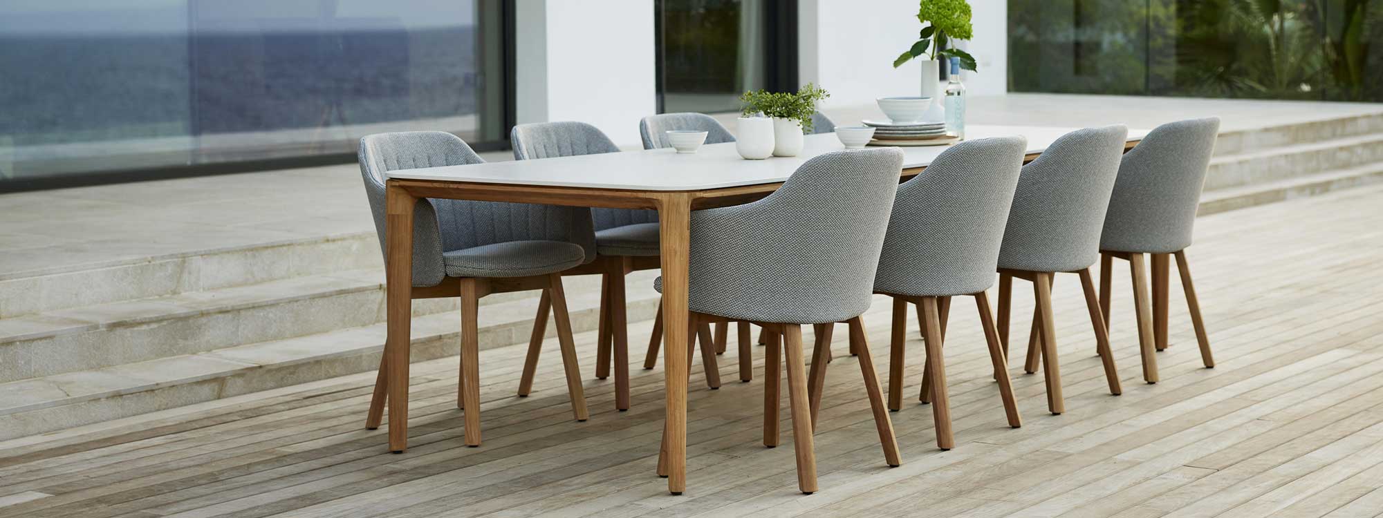 Image of Choice teak garden chairs with light-grey seat and back upholstery, together with Aspect teak table with Travertine ceramic top by Cane-line