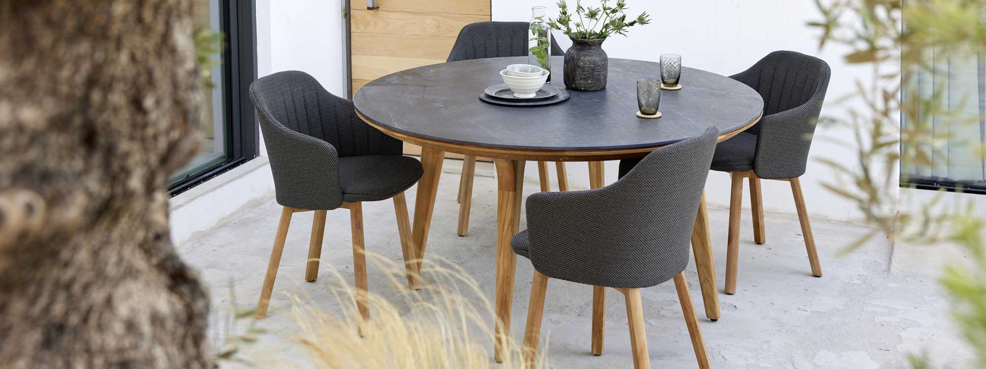 Image of Aspect round teak table with Black Volcano ceramic & Choice teak chairs with dark-grey seat and back upholstery by Cane-line