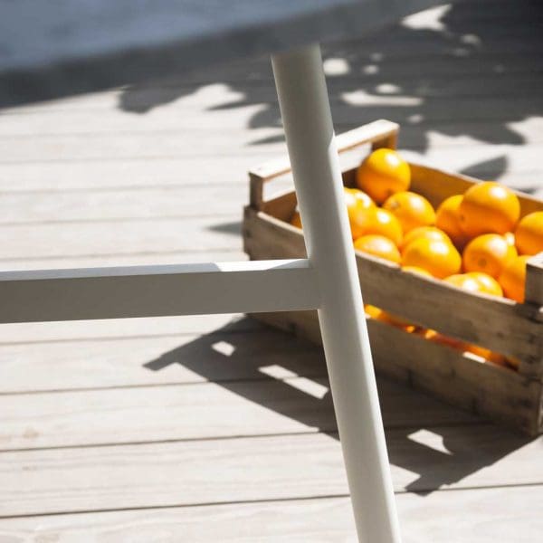 Image of detail of white tubular stainless steel leg of Gamma modern garden table by RODA, with box of oranges on the floor in the background