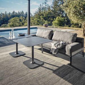 Image of Gloster Grid grey garden dining sofa and dining tables with Nero ceramic table tops, with swimming pool in the background