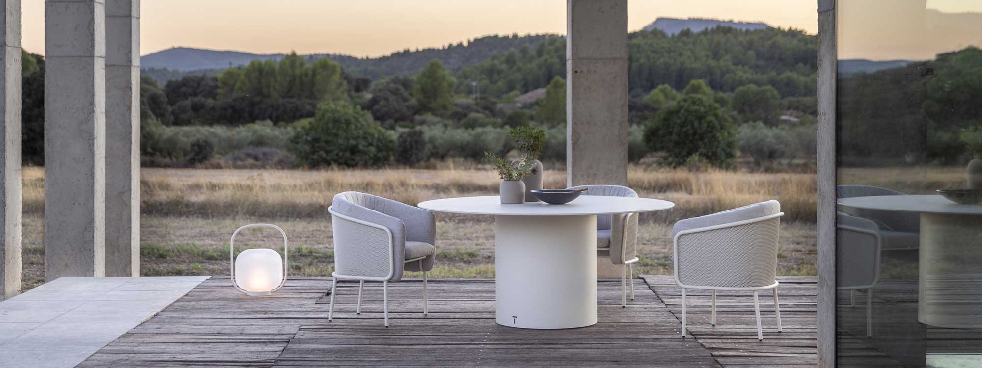 Image of Slide white upholstered garden chairs and Branta white round garden table by Todus on wooden decking at dusk