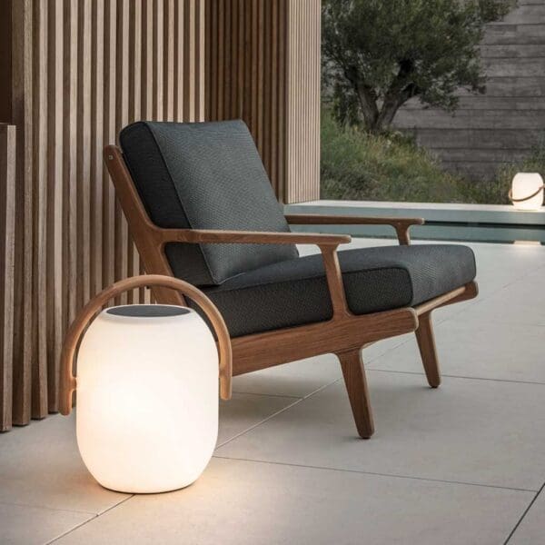 Image of Gloster Bay retro teak garden lounge chair with grey cushions and Lantern modern garden light