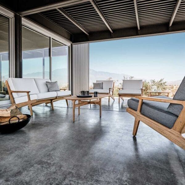 Image of Bay modern teak garden lounge furniture with white and grey cushions by Gloster, shown on poured concrete terrace