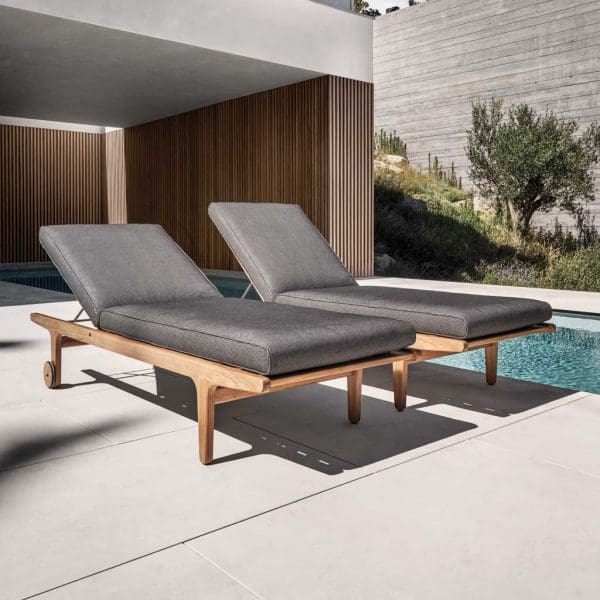 Image of pair of Gloster Bay adjustable teak sunbeds on sunny poolside terrace, with brutalist architecture in the background