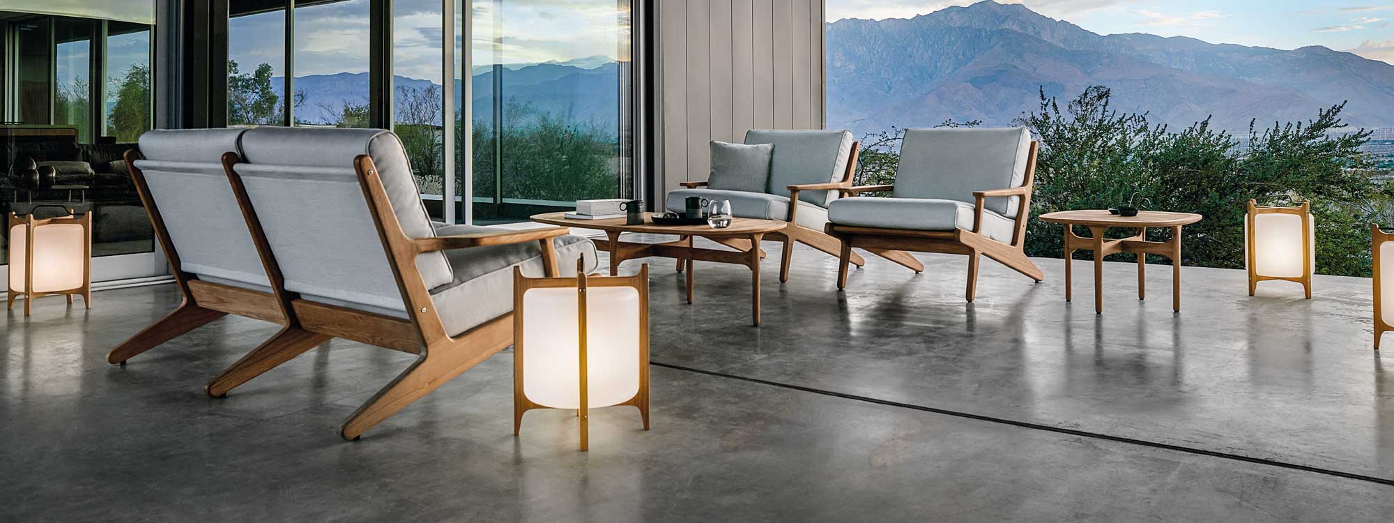 Image of Gloster Bay teak sofa and lounge chairs, together with Lantern modern lights, on poured concrete terrace with mountainous countryside in the background