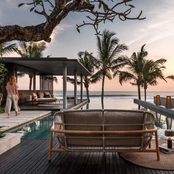 Image at dusk of Gloster Fern double garden sofa with palm trees and sea in the background